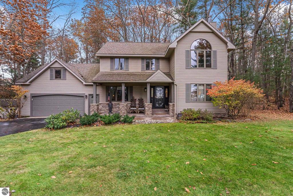 Modern two-story home with a stone-accented porch, surrounded by trees and colorful autumn foliage, located at 5347 Birch Glen Road, Lake Ann, MI, emphasizing its blend of luxury and nature.