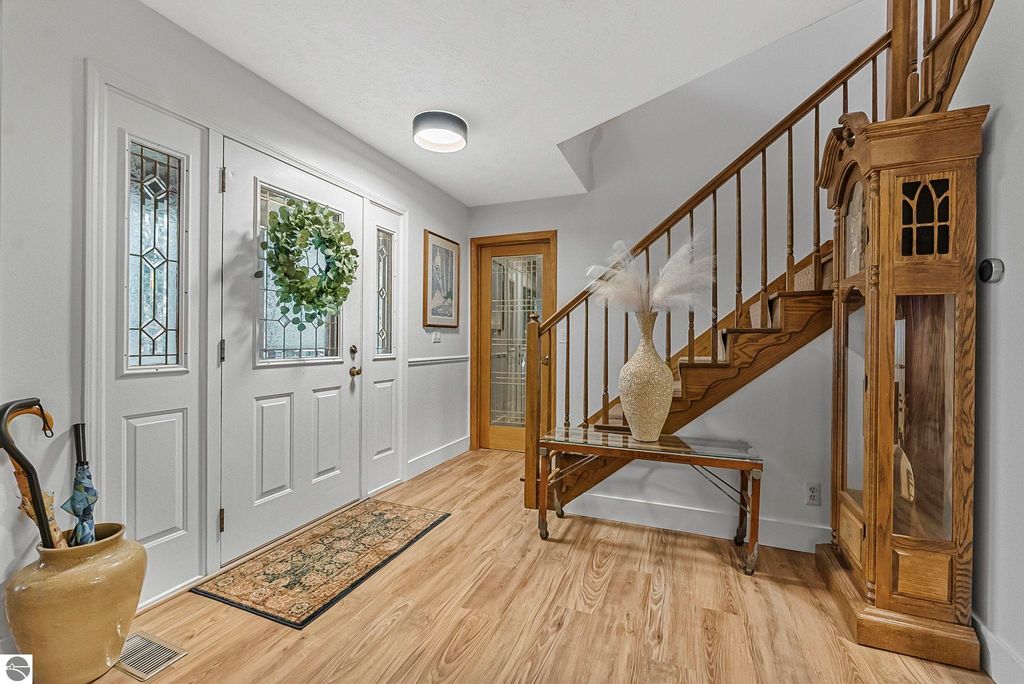 Welcoming entryway of a luxury home featuring a decorative wreath on the front door, wooden staircase, and elegant furnishings, showcasing modern interior design elements.
