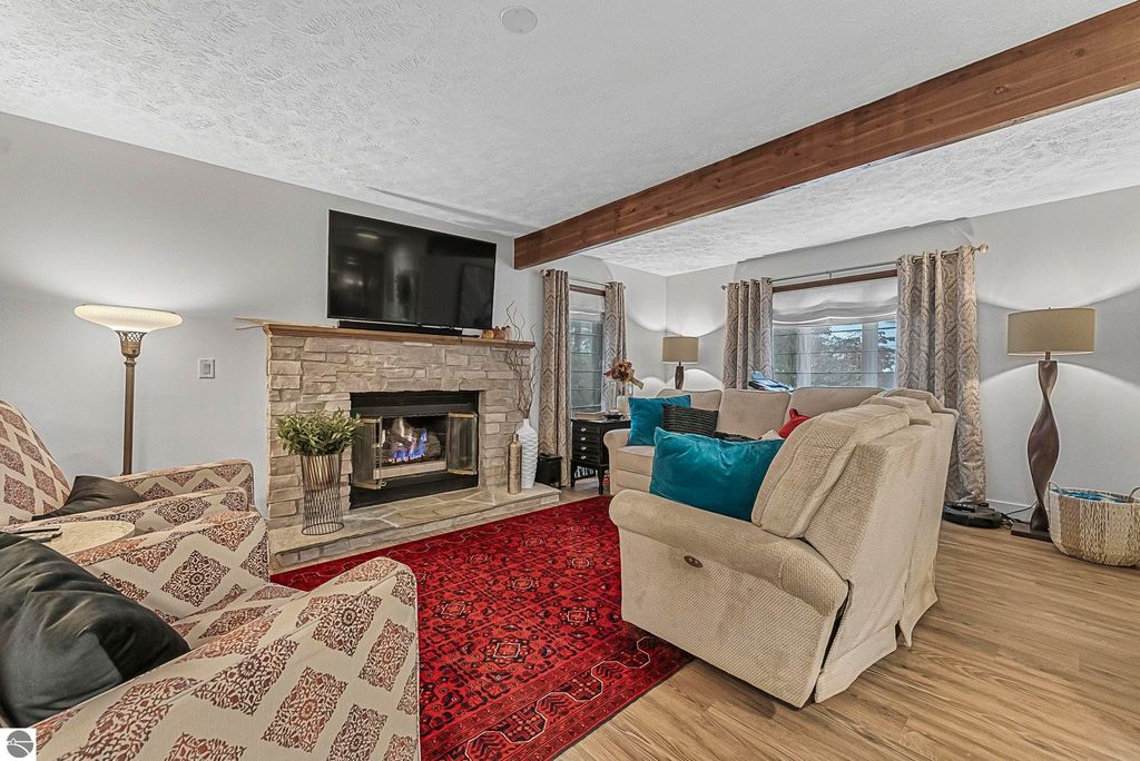 Cozy living room featuring a stone fireplace, modern TV, and comfortable seating with colorful accents, set in a fully renovated home at 5347 Birch Glen Road, Lake Ann, MI.