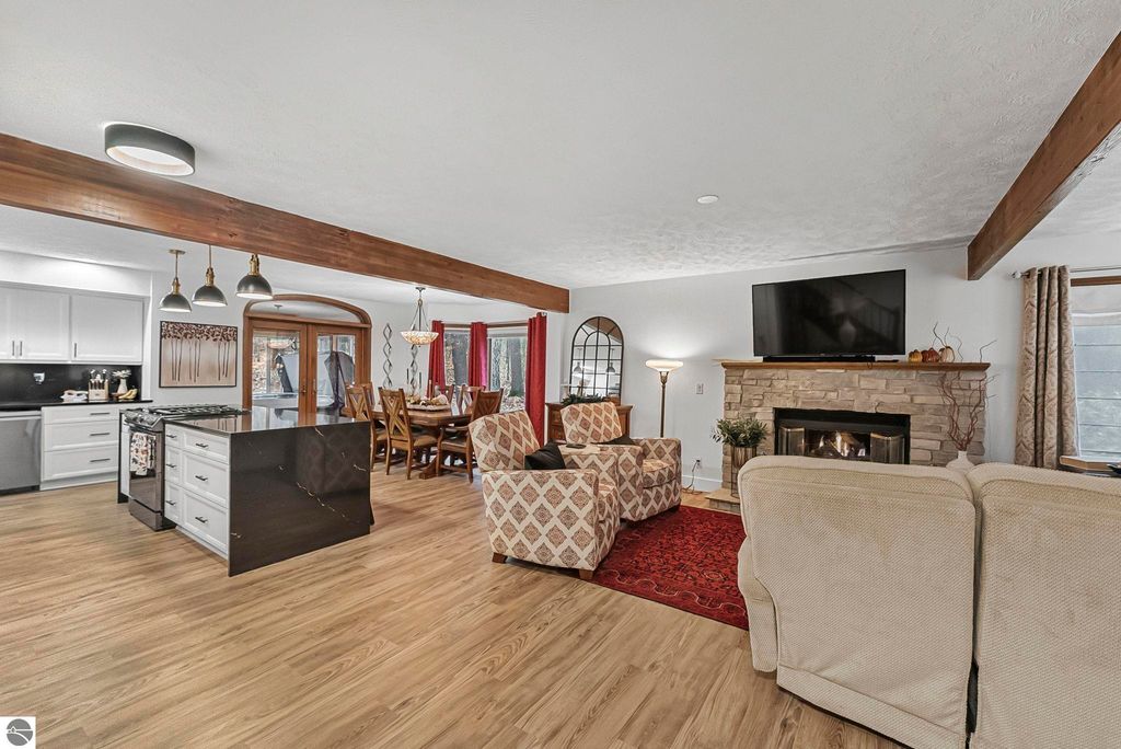 Modern living room featuring cozy seating, stone fireplace, and open kitchen, showcasing luxury home design at 5347 Birch Glen Road, Lake Ann, MI.