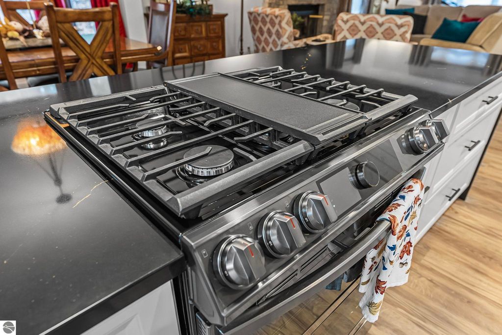 Chef's kitchen featuring a premium gas range with black quartz countertops, decorative kitchen towel, and modern design elements in a spacious living area.