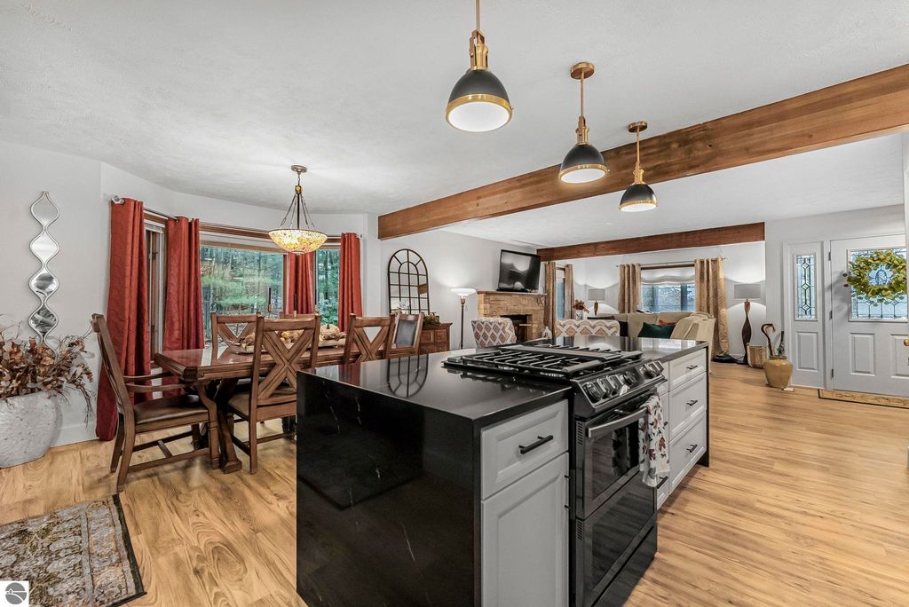Modern kitchen and dining area featuring black quartz countertops, wooden dining table, and large windows with forest views, showcasing a blend of luxury and rustic charm in a Lake Ann home.