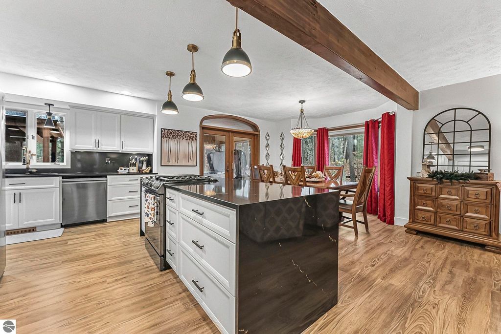 Modern kitchen featuring sleek white cabinetry, black quartz countertops, premium gas range, and spacious dining area with red curtains and wooden accents, ideal for entertaining in a Lake Ann luxury home.