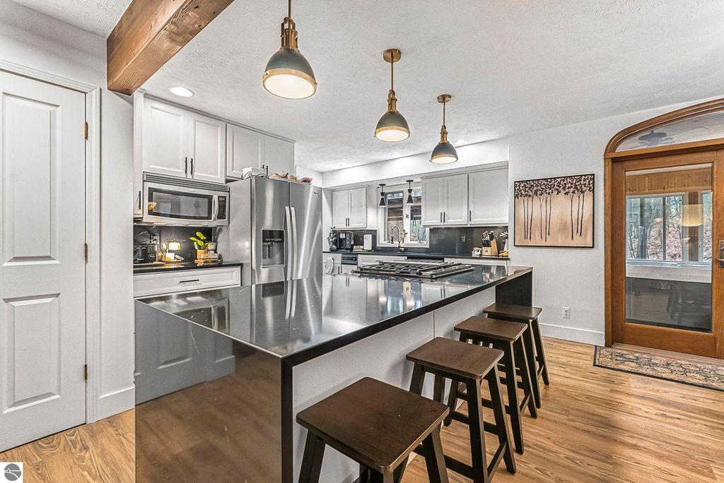 Modern kitchen with stainless steel appliances, black quartz countertops, and a spacious island with seating, showcasing a blend of luxury and functionality in a Lake Ann home.
