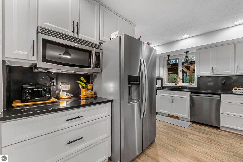 Modern kitchen interior featuring stainless steel appliances, including a refrigerator and microwave, black quartz countertops, and white cabinetry, designed for a luxury home in Lake Ann, MI.