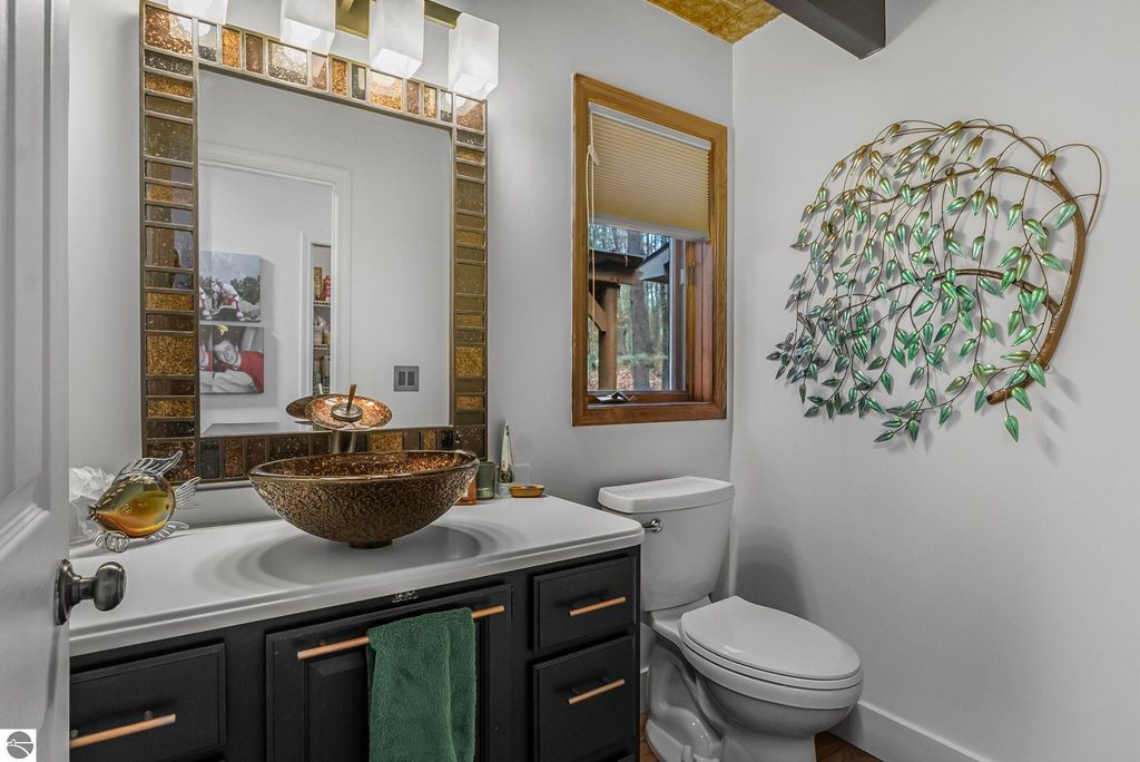 Luxurious bathroom featuring a stylish vessel sink, modern fixtures, decorative mosaic mirror, and nature-inspired wall art, set in a contemporary home in Lake Ann, MI.