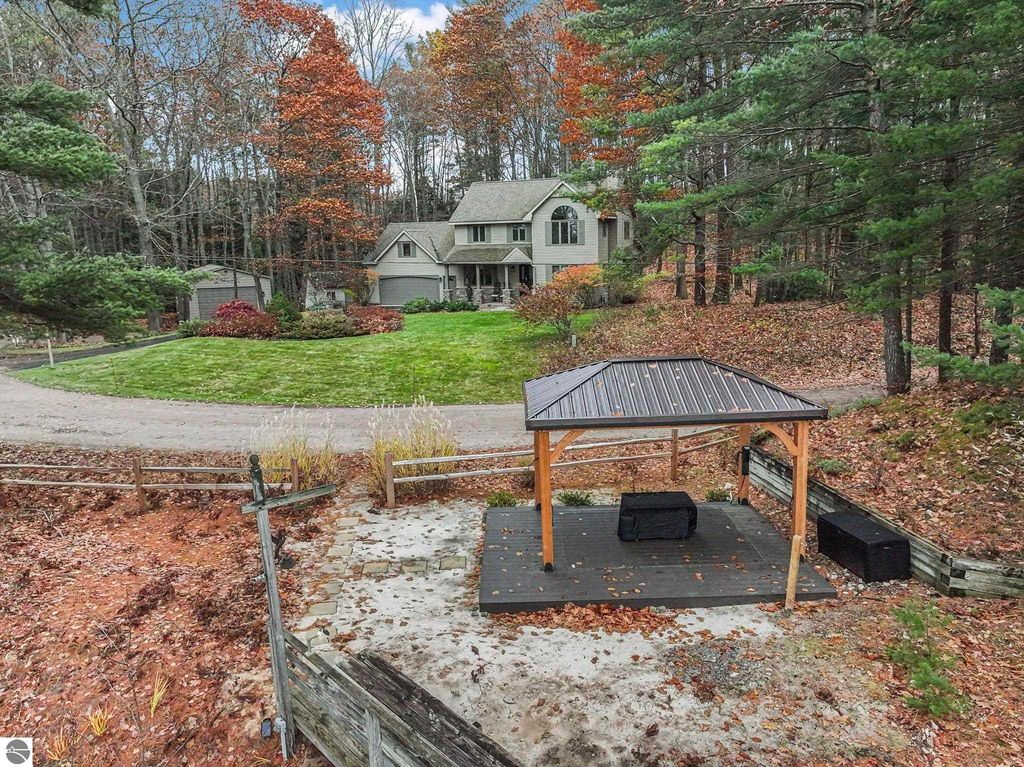 Modern luxury home at 5347 Birch Glen Road, Lake Ann, MI, surrounded by autumn foliage, featuring a gazebo in a landscaped yard and spacious driveway.