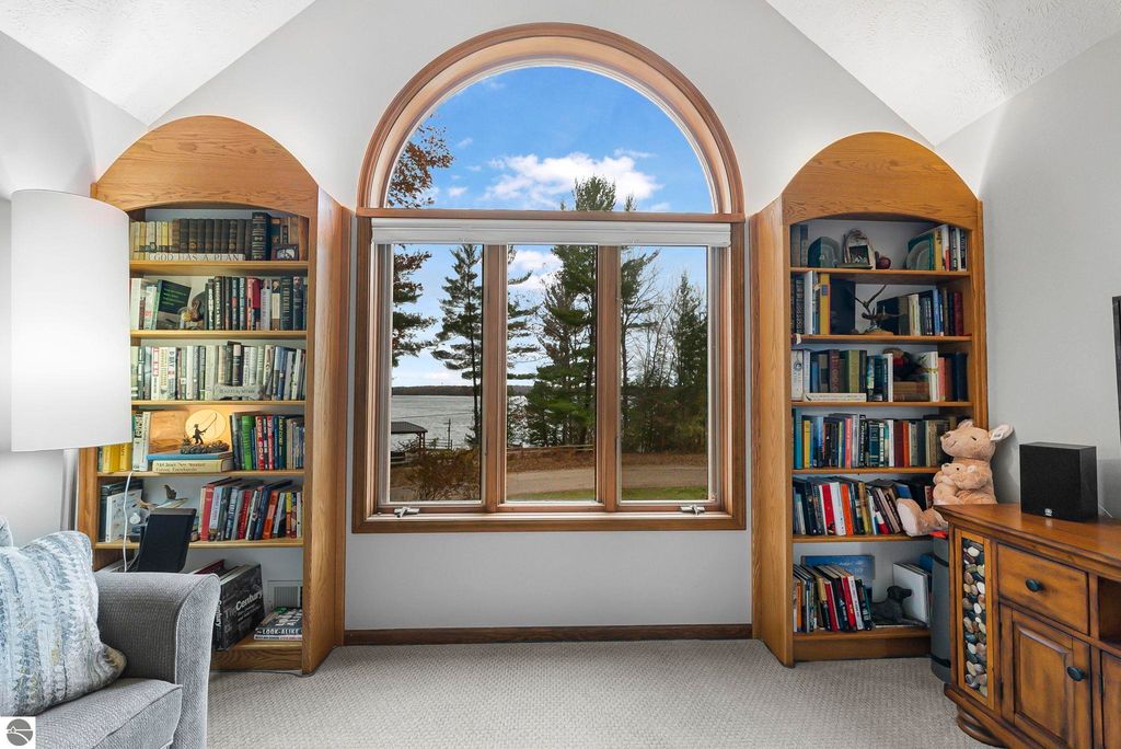 Cozy living room corner with built-in bookshelves, large arched window showcasing lake views, plush seating, and decorative lamp, emphasizing the serene ambiance of the Lake Ann home.