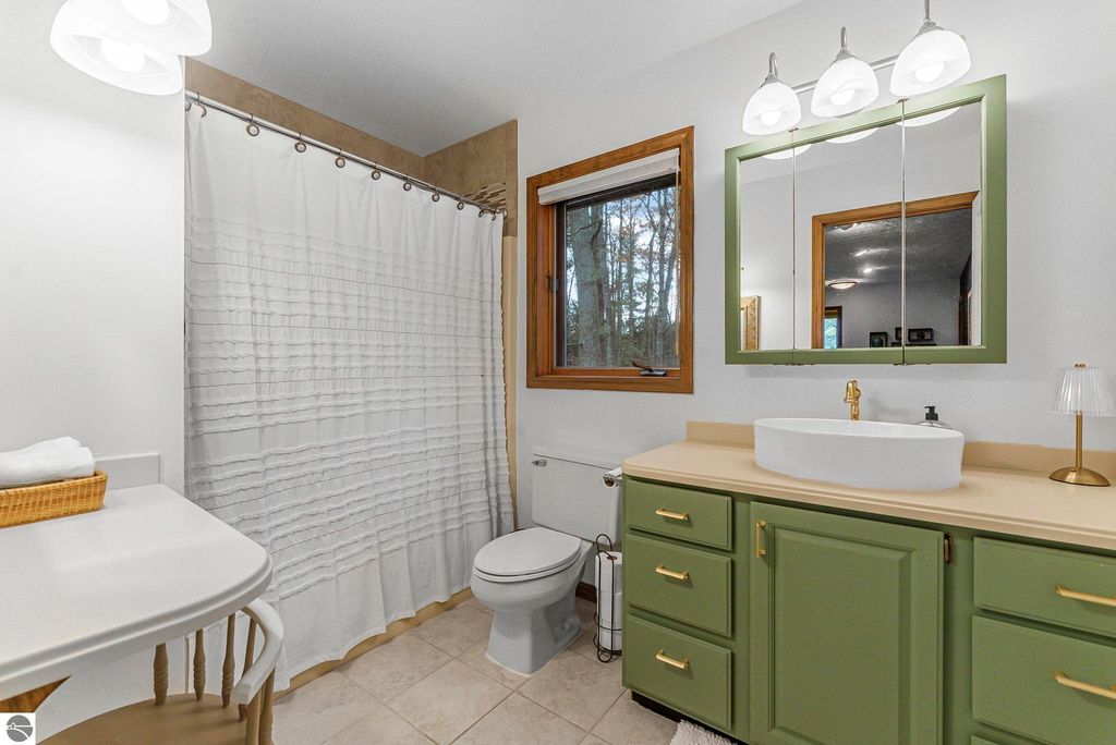 Modern bathroom featuring green cabinetry, a white sink, and a shower with a white curtain, complemented by natural light from a window overlooking wooded scenery.