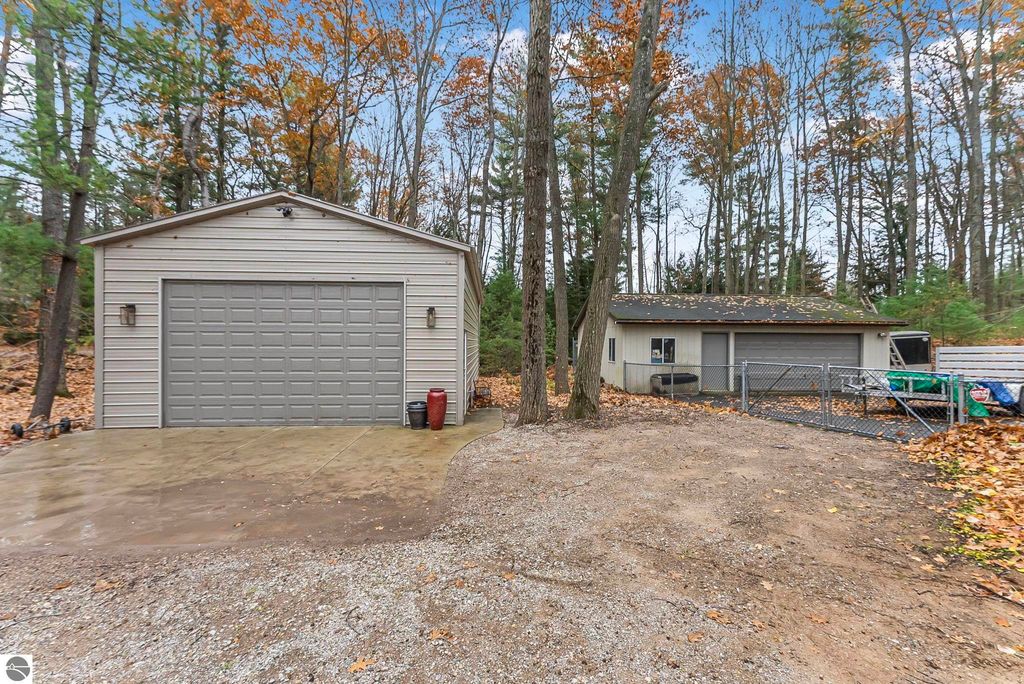 Detached garage and additional storage building on wooded property at 5347 Birch Glen Road, Lake Ann, MI, surrounded by autumn foliage.
