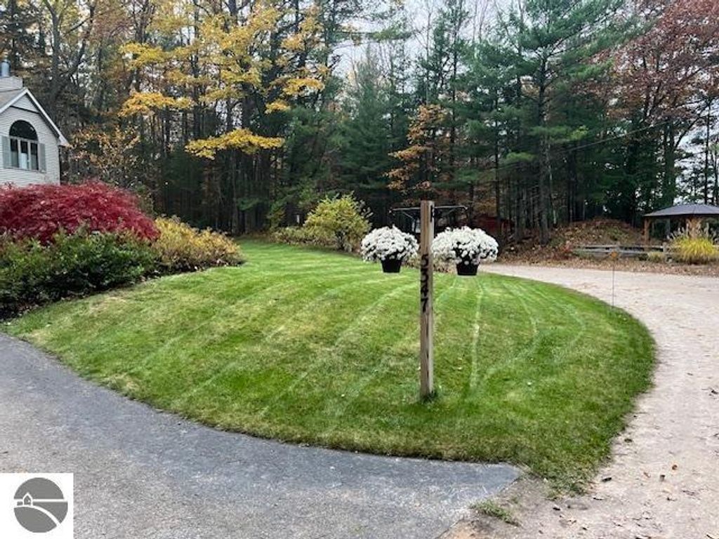 5347 Birch Glen Road entrance with manicured lawn, colorful fall foliage, and flower planters, showcasing the property&rsquo;s appeal in Lake Ann, MI.