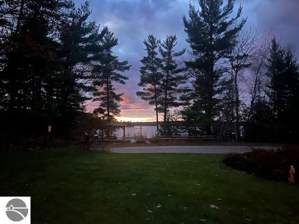 Lake Ann waterfront view at sunset, featuring trees, serene lake, and grassy foreground, highlighting the property's natural beauty and tranquility.