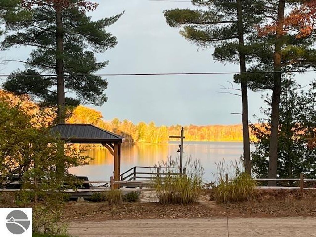 Scenic view of Lake Ann with a private dock, surrounded by trees and autumn foliage, highlighting the lakefront access of the property at 5347 Birch Glen Road, Lake Ann, MI.