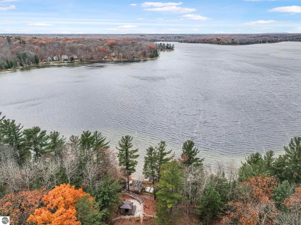 Aerial view of Lake Ann showcasing serene waters, surrounding autumn foliage, and wooded shoreline, highlighting the property at 5347 Birch Glen Road, ideal for lakefront living and outdoor activities.