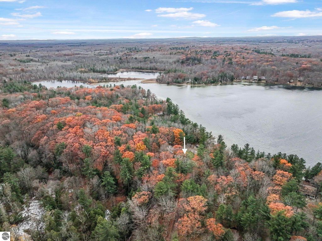 Aerial view of colorful autumn foliage surrounding Lake Ann, highlighting wooded land and lakefront property at 5347 Birch Glen Road, Lake Ann, MI.