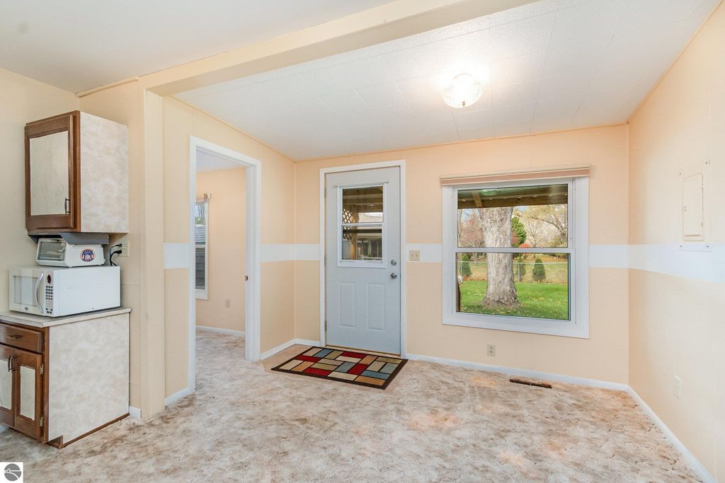 Interior view of a cozy mudroom entry with beige walls, a door leading outside, a window with a view of the yard, and a small kitchen area featuring a microwave and cabinets, showcasing the welcoming space of a 2-bedroom, 1-bath home in Mt Pleasant, MI.