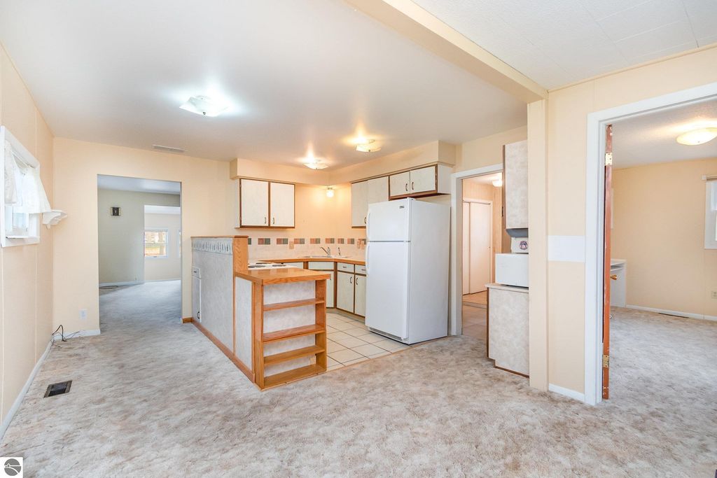 Interior view of a move-in ready 2-bedroom, 1-bath home featuring a kitchen with white appliances, light-colored cabinetry, and carpeted flooring, showcasing the layout relevant to the listing at 1435 E Broadway Street, Mt Pleasant, MI.