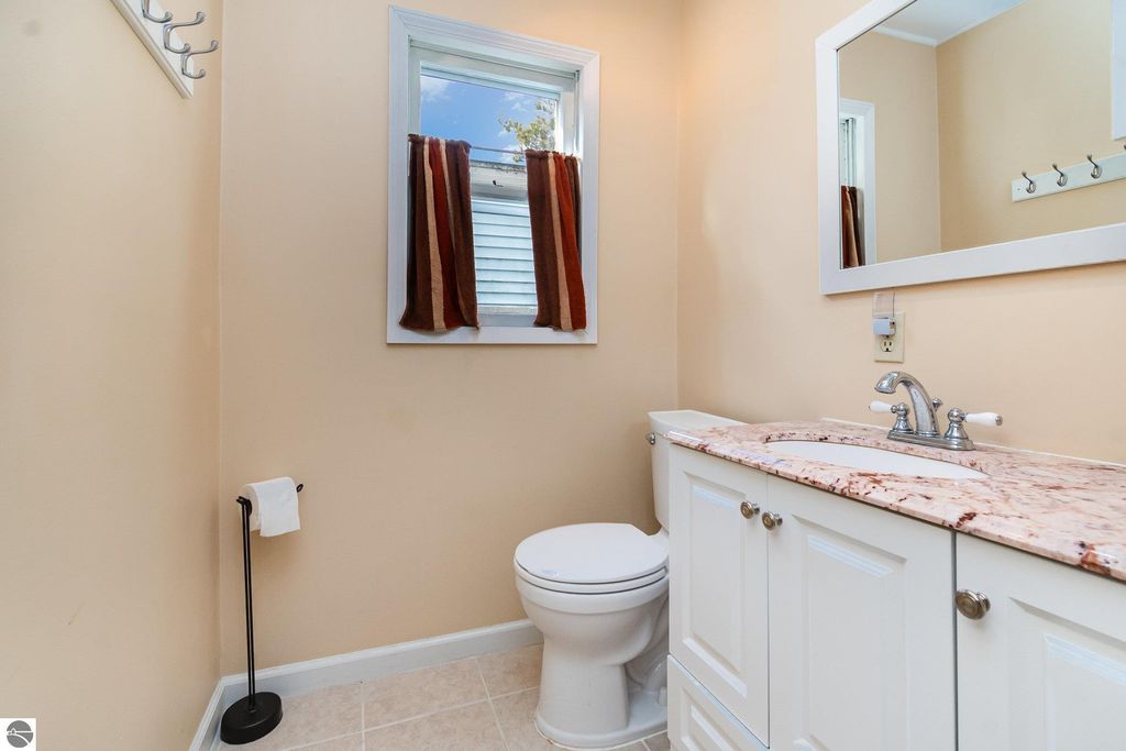 Bathroom interior featuring a white toilet, granite countertop sink with faucet, beige walls, and window with brown curtains, showcasing a clean and modern design ideal for a 2-bedroom home in Mt Pleasant, MI.