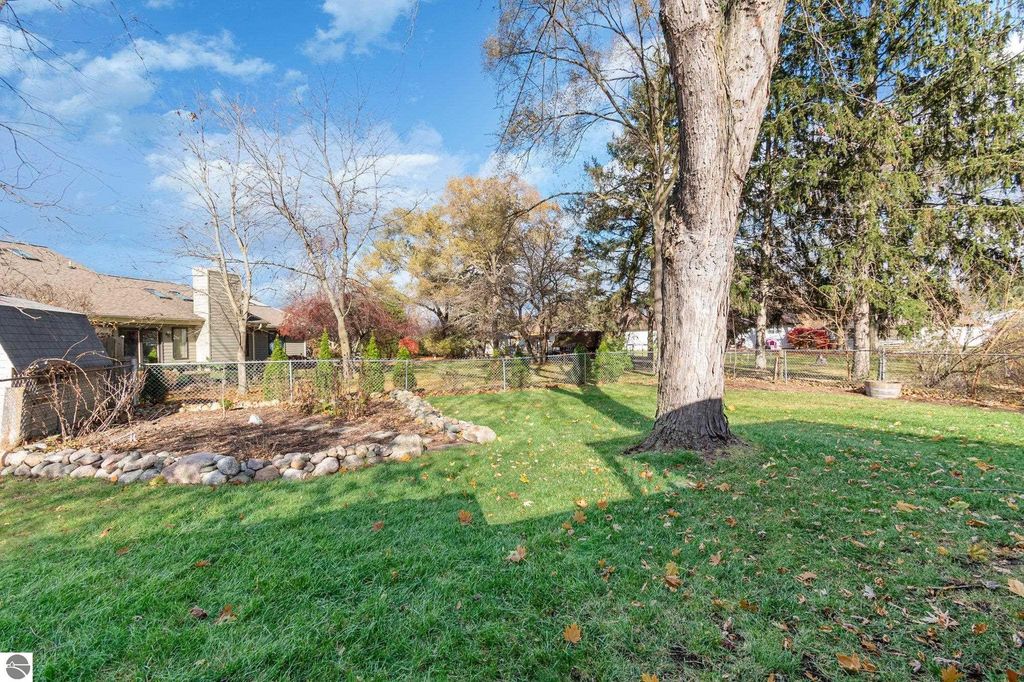Fenced backyard of 2-bedroom home at 1435 E Broadway Street, Mt Pleasant, MI, featuring a large tree, landscaped area with stones, and open green lawn, ideal for outdoor activities.