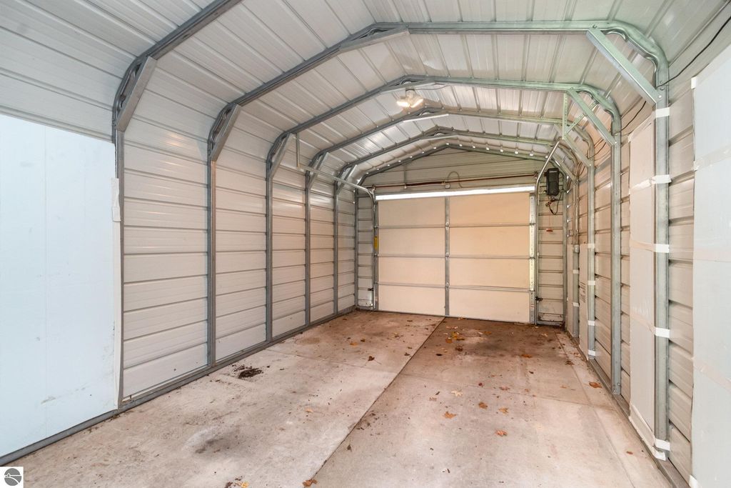 Interior view of a one-car garage with metal walls and concrete flooring, featuring an open garage door and light fixtures, showcasing the storage space available for the home at 1435 E Broadway Street, Mt Pleasant, MI.