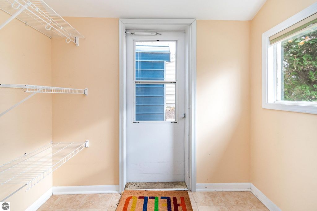 Mudroom entry of a 2-bedroom home in Mt Pleasant, MI, featuring a door leading outside, a window, and wire shelving, with a colorful welcome mat.