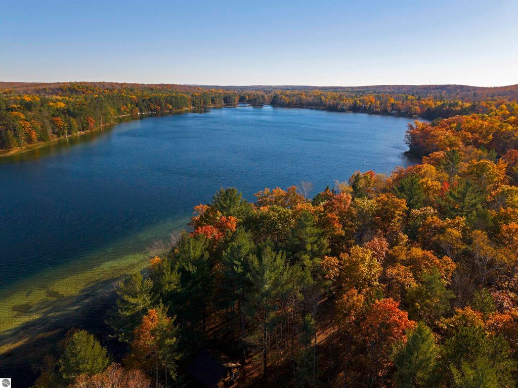 Aerial view of Pickerel Lake surrounded by vibrant autumn foliage, showcasing the clear blue water and lush greenery, ideal for a dream home or getaway near Kalkaska, MI.