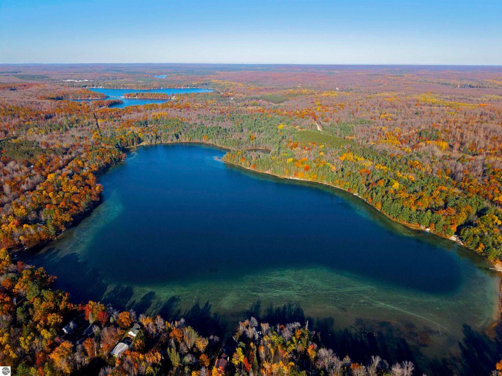 Aerial view of Pickerel Lake surrounded by vibrant autumn foliage, showcasing clear blue-green water and wooded shoreline, ideal for building a dream home or getaway near Kalkaska, MI.