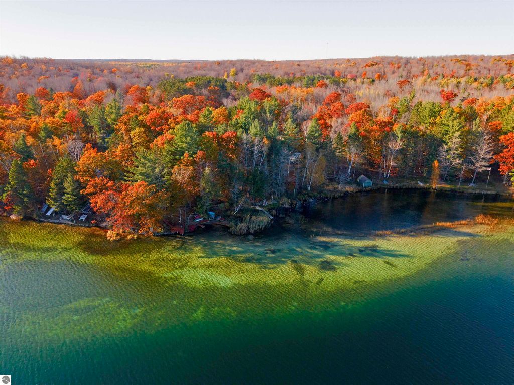 Aerial view of Pickerel Lake surrounded by vibrant autumn foliage, showcasing clear blue-green waters and wooded shoreline, ideal for building a dream home or getaway in Kalkaska, MI.