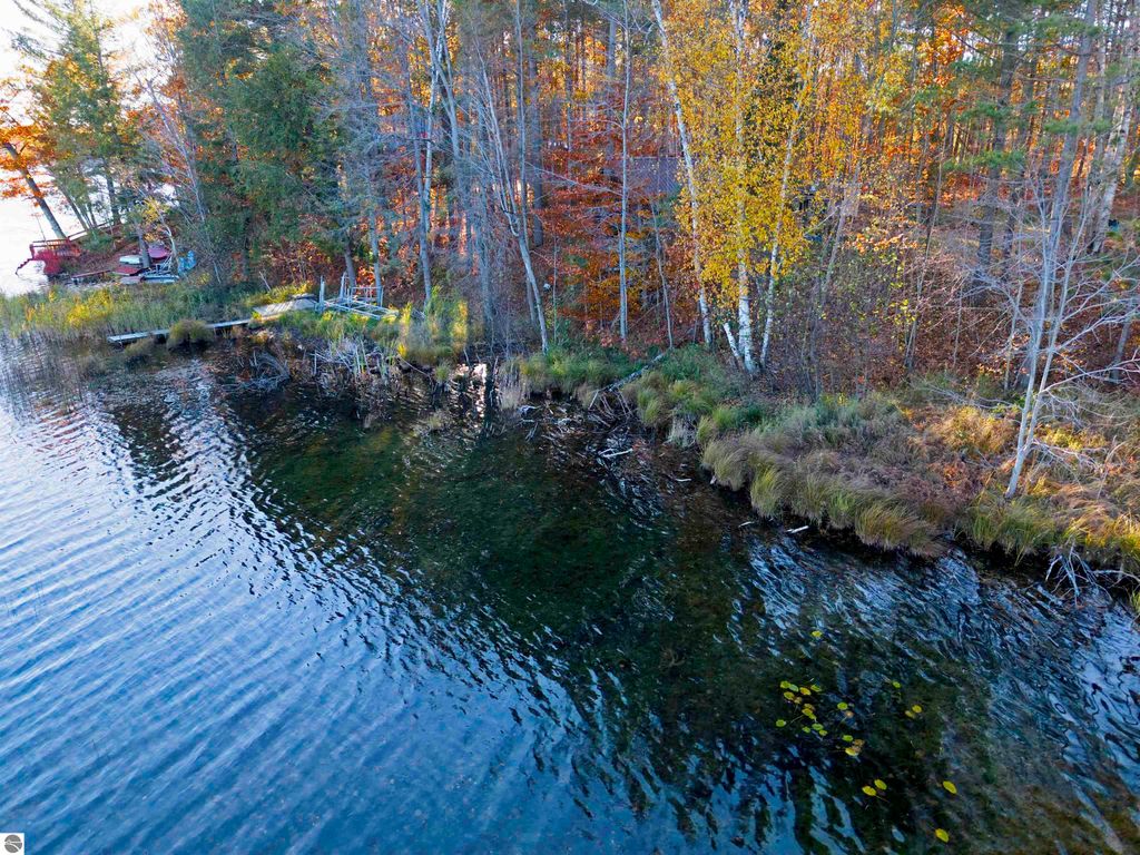 Scenic waterfront view of Pickerel Lake shoreline, featuring autumn foliage, grassy edges, and a small dock, ideal for building a dream home or getaway near Kalkaska, MI.