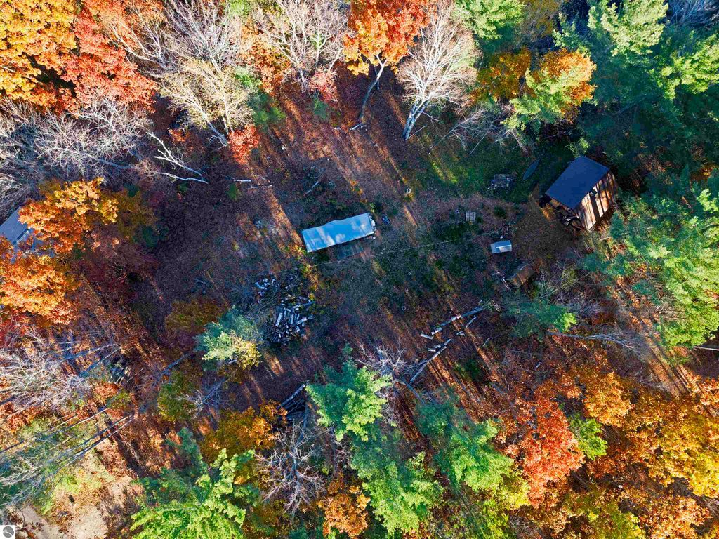 Aerial view of wooded land with vibrant fall foliage, featuring an older cabin and clearing for building near Pickerel Lake, ideal for recreational activities.