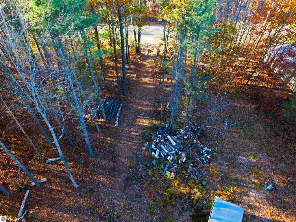 Aerial view of wooded land at 6320 Woodland Drive NE, Kalkaska, MI, showcasing tree-lined path and pile of logs, ideal for building a dream home near Pickerel Lake.