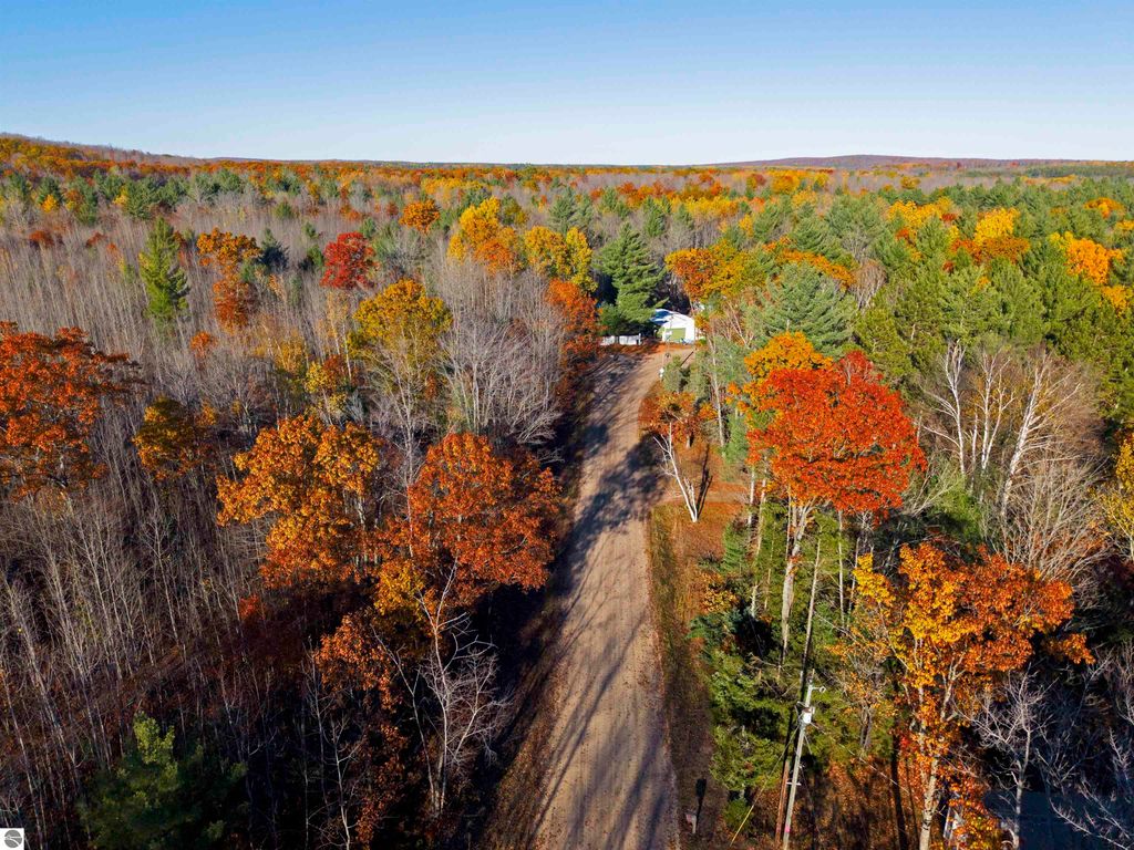 Aerial view of a wooded area with vibrant autumn foliage, featuring a dirt road leading to a cabin, highlighting the serene and private setting ideal for a getaway near Pickerel Lake in Kalkaska, MI.