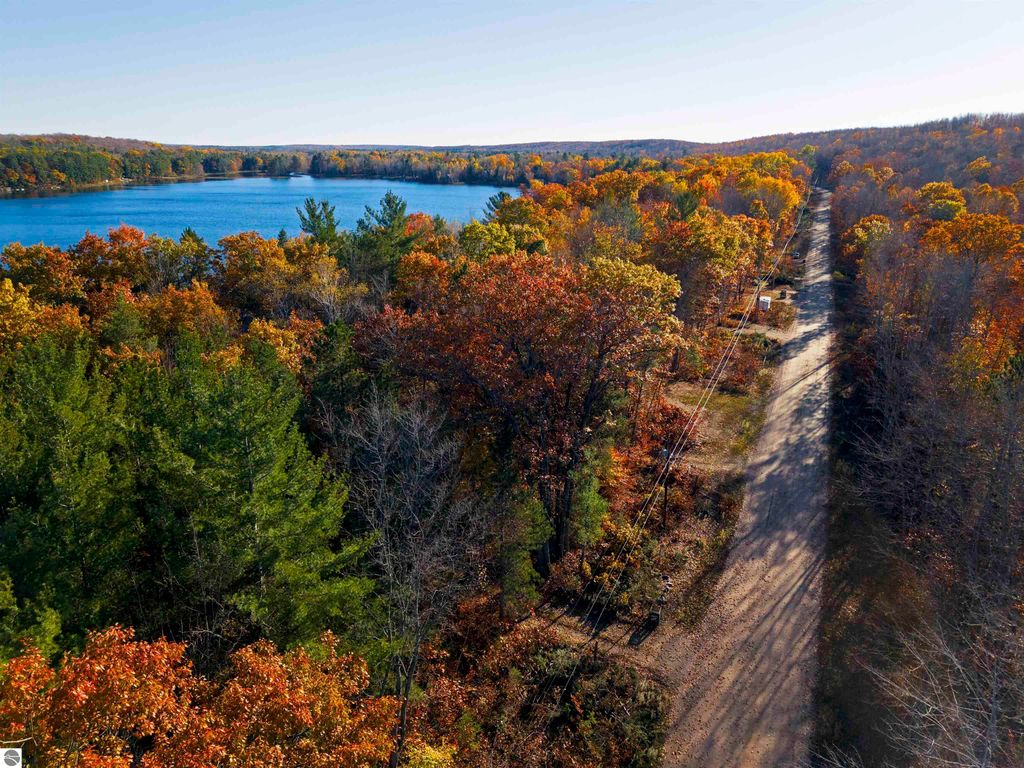 Aerial view of vibrant autumn foliage along a dirt road leading to Pickerel Lake, showcasing a serene waterfront property in Kalkaska, MI, ideal for building a dream home or getaway.