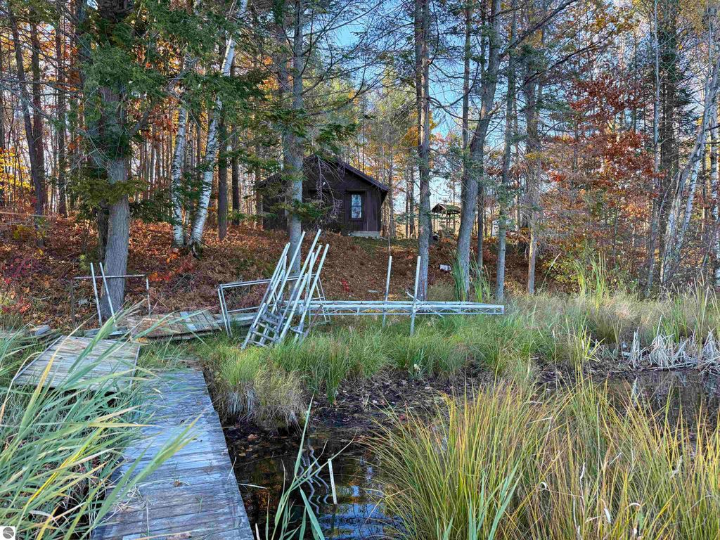 Dock leading to Pickerel Lake with an older cabin nestled among trees, showcasing a serene waterfront setting ideal for building a dream home or getaway in Kalkaska, MI.