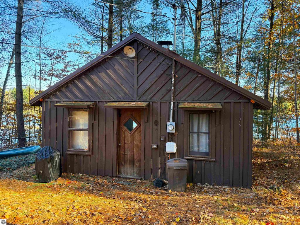Older cabin on waterfront property at 6320 Woodland Drive NE, surrounded by trees and autumn foliage, featuring a brown wooden exterior, electric meter, and views of Pickerel Lake.