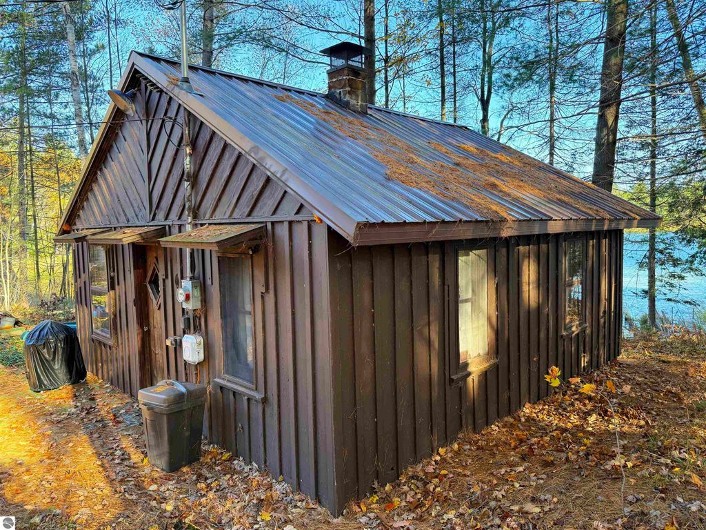Older cabin with brown wooden exterior, metal roof, and nearby Pickerel Lake, surrounded by trees and autumn foliage, ideal for a getaway or new home site.