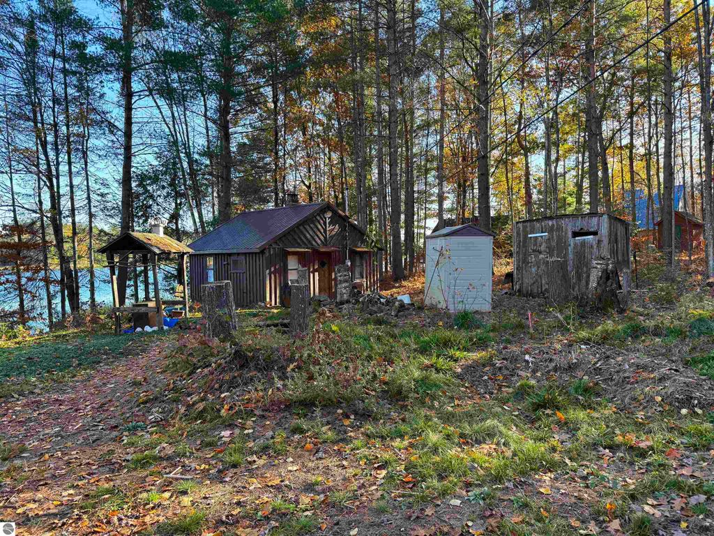 Older cabin near Pickerel Lake with surrounding trees, outdoor storage shed, and scenic waterfront view, ideal for building a dream home or getaway.
