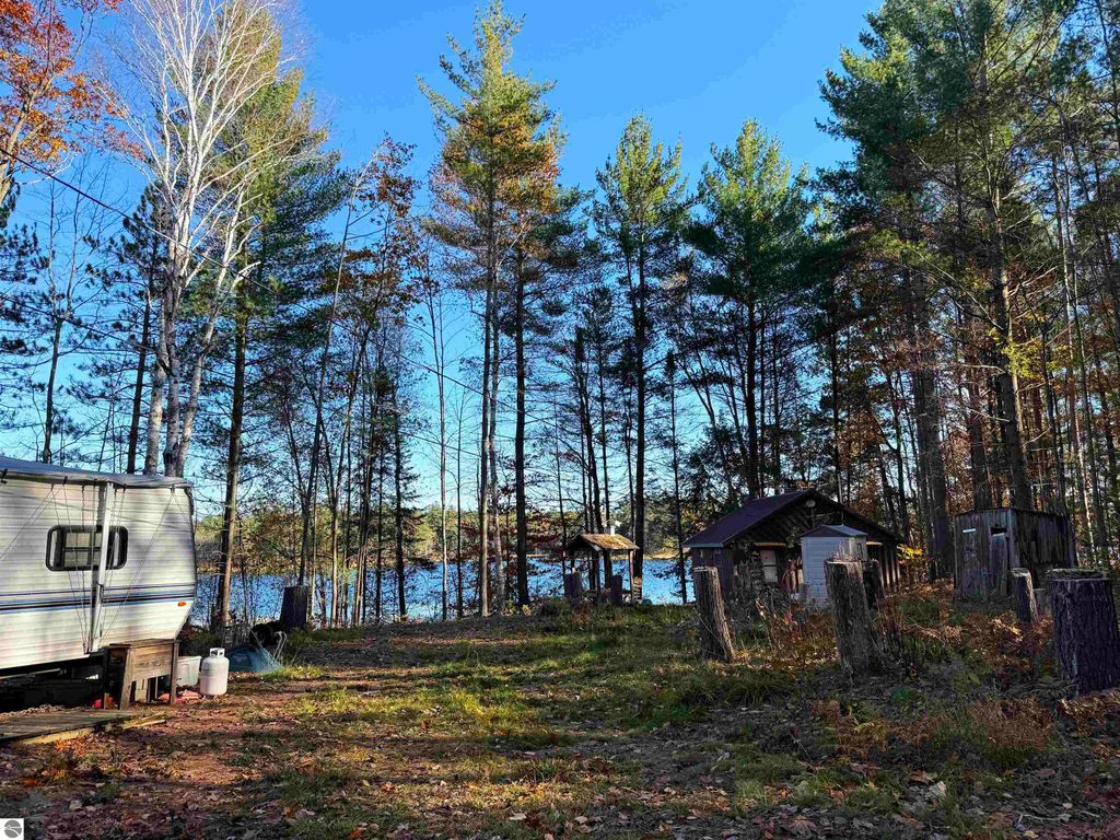 Scenic view of a wooded area near Pickerel Lake, featuring a camper and an older cabin, surrounded by tall trees and autumn foliage, ideal for building a dream home or getaway.