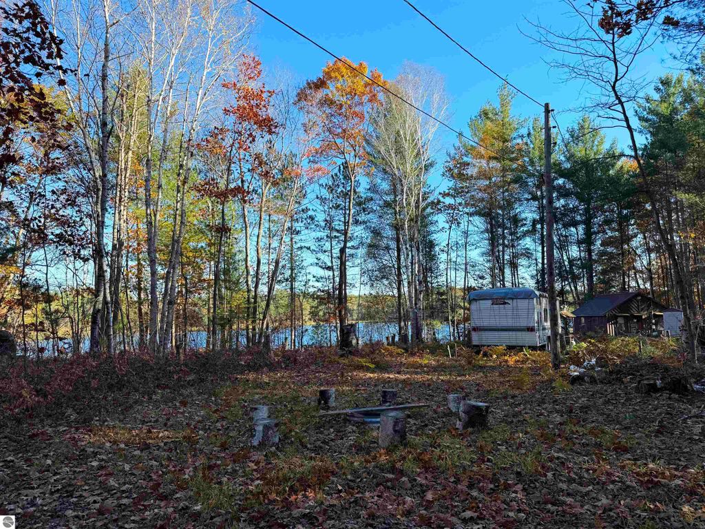 Scenic view of wooded land at 6320 Woodland Drive NE, featuring a clearing with a fire pit, older cabin, and proximity to Pickerel Lake, ideal for building a dream home or getaway.