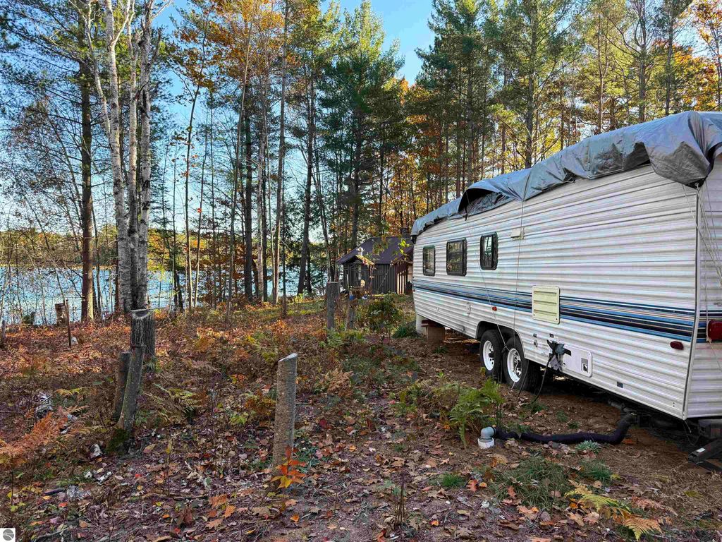 Camper trailer nestled among trees near Pickerel Lake, showcasing autumn foliage and a serene waterfront setting, ideal for building a dream home or getaway.