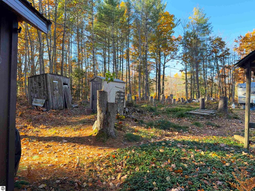 Wooded lot with autumn foliage, featuring older cabins and a trailer, ideal for building a dream home near Pickerel Lake in Kalkaska, MI.