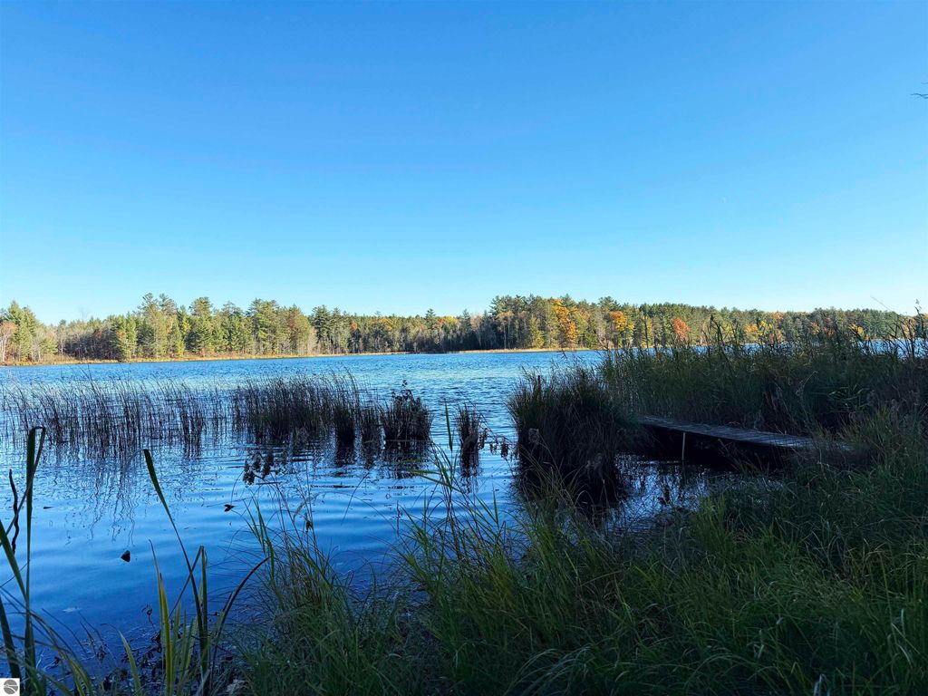 Scenic view of Pickerel Lake with clear blue water, surrounded by lush greenery and autumn-colored trees, ideal for building a dream home or getaway near Kalkaska, MI.