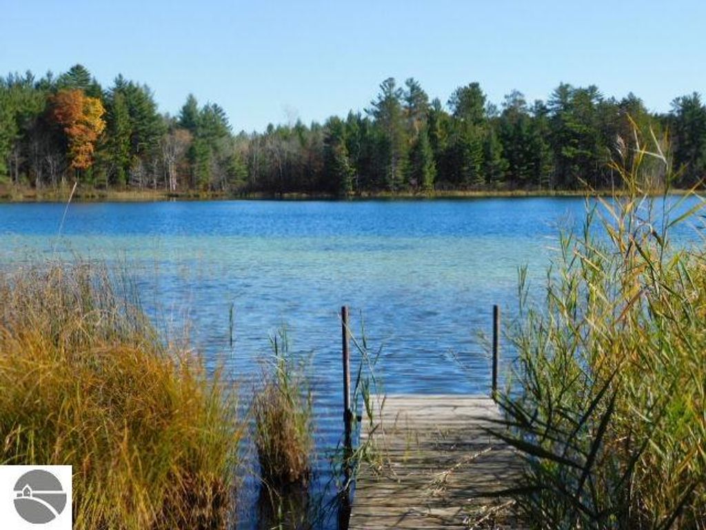 Scenic view of Pickerel Lake with a wooden dock, surrounded by lush greenery and colorful autumn foliage, highlighting the waterfront property at 6320 Woodland Drive NE, Kalkaska, MI.