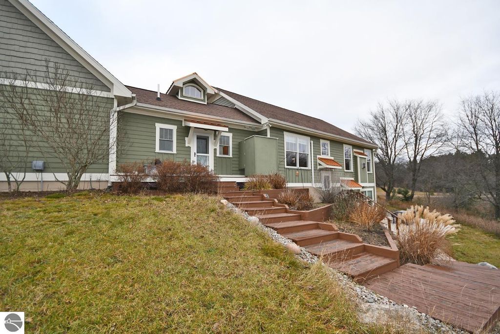 Exterior view of the home at 11007 S Rolling Meadows Drive, showcasing a green facade, multiple windows, and landscaped steps leading to the entrance, set on a rolling hillside in Maple City, MI.