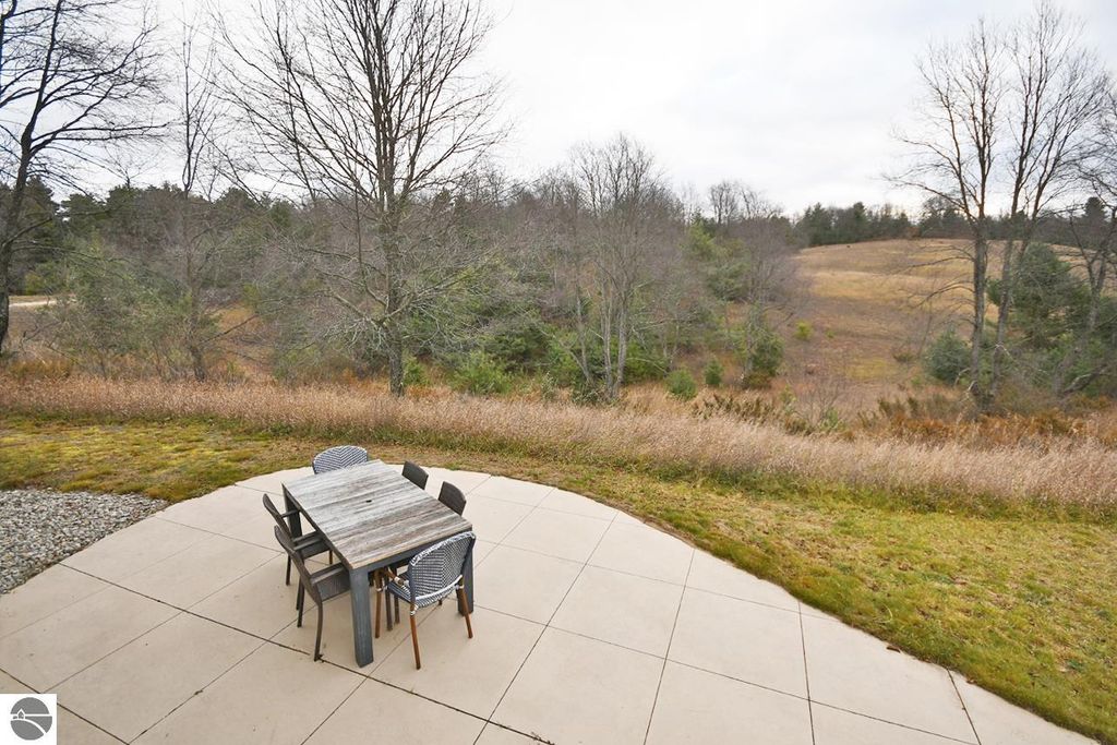 Outdoor patio with dining table and chairs overlooking rolling hills and meadows at 11007 S Rolling Meadows Drive, Maple City, MI, showcasing the property's serene homestead lifestyle.