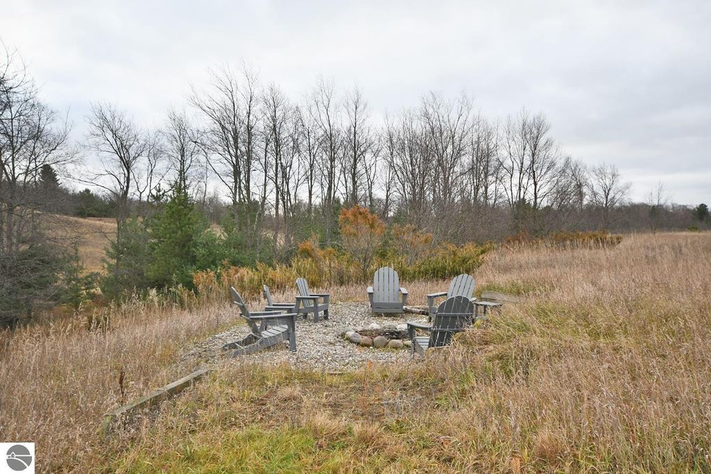 Fire pit area with Adirondack chairs surrounded by tall grass and trees, showcasing the serene outdoor space on the 9.9-acre property at 11007 S Rolling Meadows Drive, Maple City, MI.