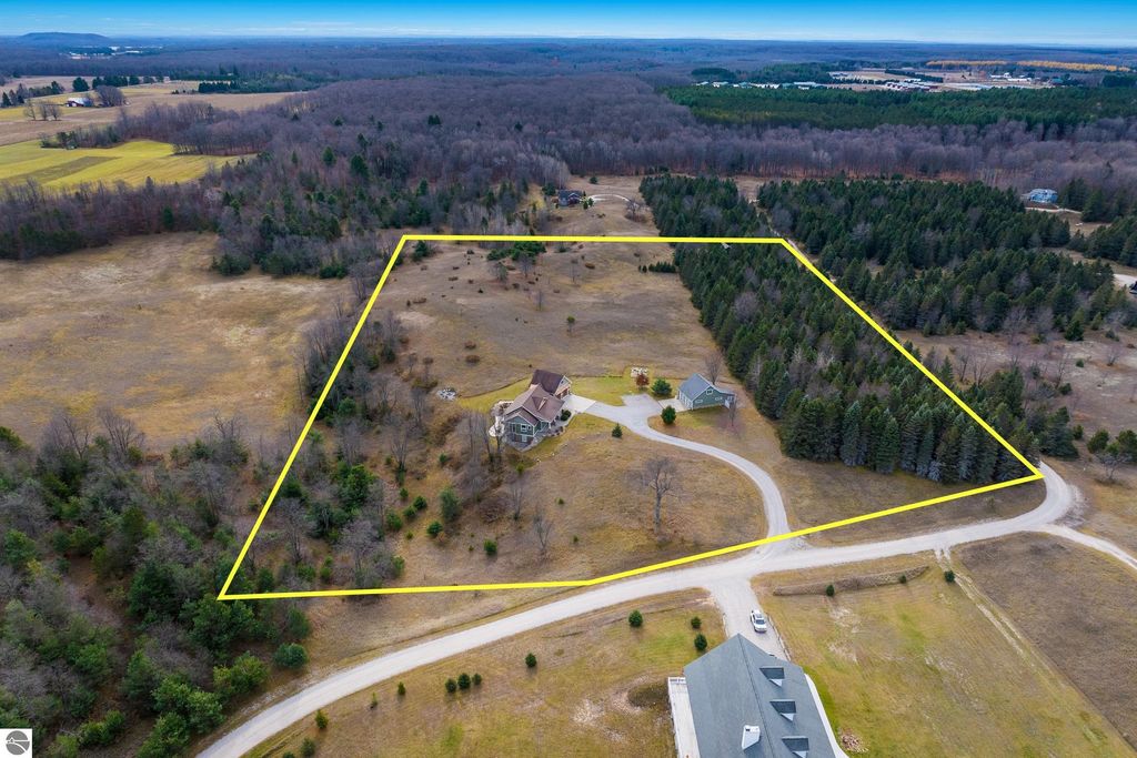Aerial view of a spacious 10-acre property in Maple City, MI, featuring a large home and surrounding landscape of rolling hills and trees, highlighting the tranquil rural setting ideal for a homestead lifestyle.
