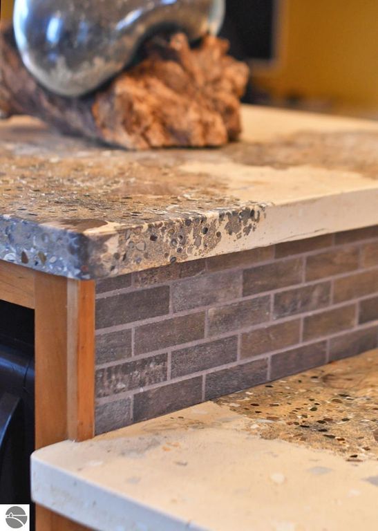 Countertop featuring textured stone and concrete surfaces, complemented by a wooden base and decorative natural elements, reflecting the high-end craftsmanship of the home's kitchen in Maple City, MI.