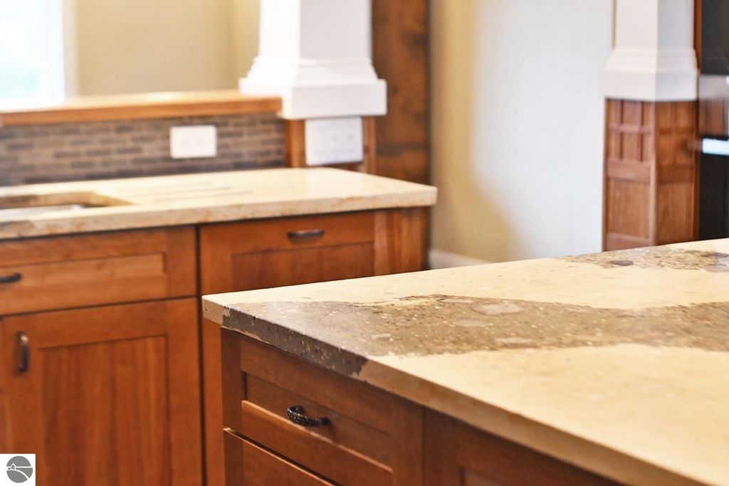 Kitchen countertop with stone and concrete surfaces, wooden cabinets, and a glimpse of a modern kitchen layout, highlighting the craftsmanship and design details of the property at 11007 S Rolling Meadows Drive, Maple City, MI.