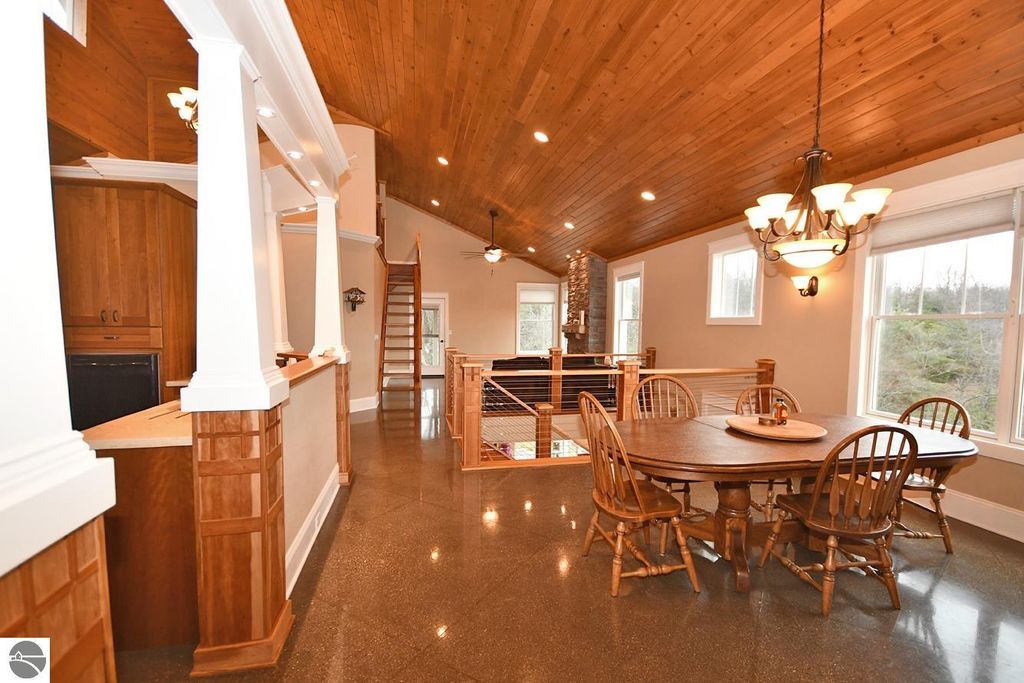 Interior view of a spacious dining area featuring a round wooden table with chairs, vaulted wood ceiling, and large windows, showcasing the open floor plan of the four-bedroom home at 11007 S Rolling Meadows Drive, Maple City, MI.